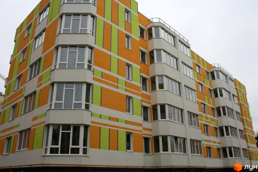 Зовнішній вигляд будинку ЖК Позитив з яскравим фасадом в оранжево-зелених тонах. Багатоквартирний будинок з великою кількістю вікон та балконів.