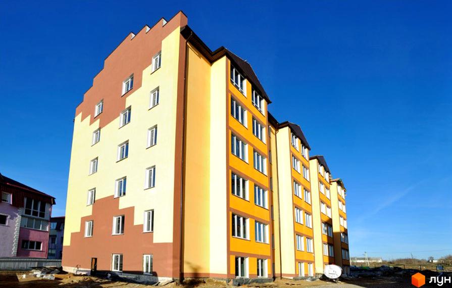 Багатоповерховий будинок з жовтим та коричневим фасадом на тлі блакитного неба. Поруч з будинком розташована прибудинкова територія.