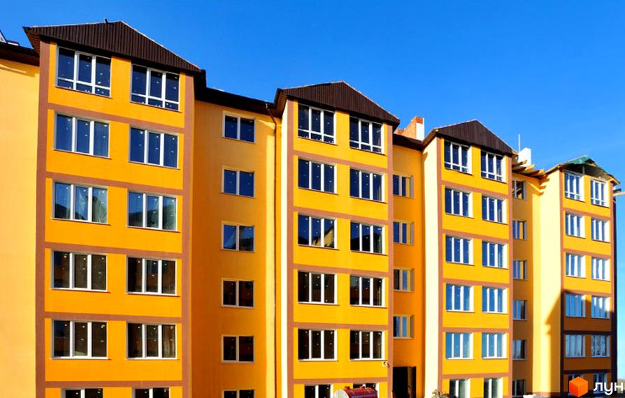 Яскравий житловий комплекс з жовтим фасадом та коричневим дахом. Багатоповерхові будинки з великою кількістю вікон на тлі блакитного неба.