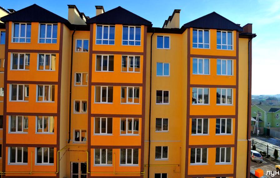 Житловий комплекс Спутник. Багатоповерховий будинок з жовтим фасадом та коричневими вставками. На даху чорна черепиця. Навколо будинку блакитне небо.