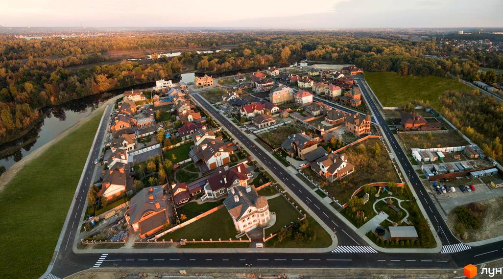 Вигляд з висоти на Котеджне містечко Коник з будинками з червоними дахами. Навколо зелені газони, дороги та ліс.