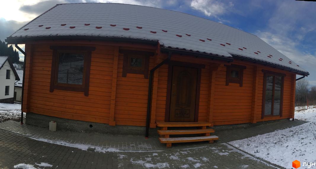 Дерев'яний будинок з помаранчевими стінами та снігом на даху. Навколо будинку засніжена територія з бруківкою.