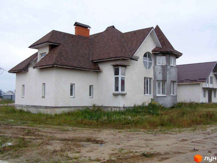 Зображення будинку в Котеджному містечку Злата Рудня. Двоповерховий будинок з коричневою черепицею та білими стінами, розташований на ділянці з травою та піщаною дорогою.