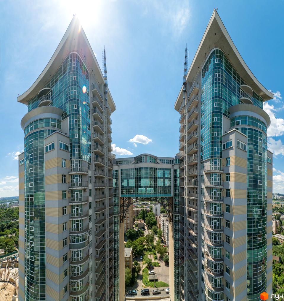 Житловий комплекс Тріумф: дві висотні будівлі з скляними фасадами та гострими дахами, з'єднані переходом. Навколо зелена територія.