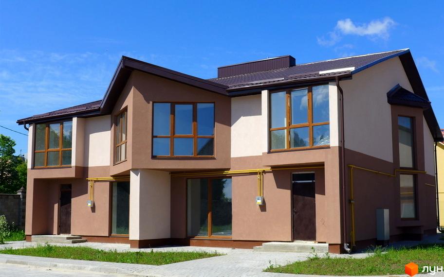 Зображення сторінки житлового комплексу Таунхауси „Княжий“. Двоповерховий будинок з великими вікнами та коричневим дахом. Перед будинком газон та тротуар.