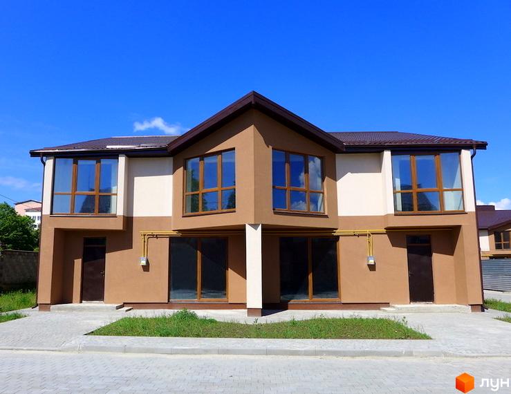 Двоповерховий таунхаус з великими вікнами та коричневим дахом. Перед будинком бруківка та невелика галявина з травою.