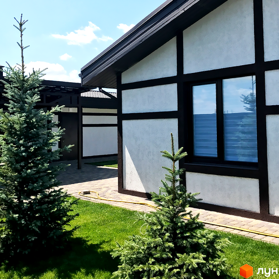 Будинок в Котеджному містечку Європейський квартал з білими стінами та темними балками. На передньому плані зелена трава та ялинки.