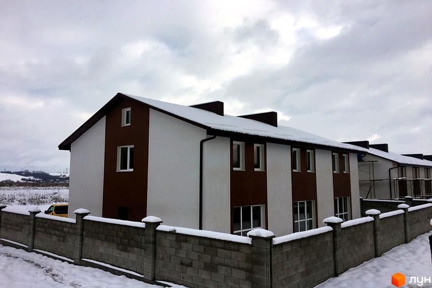Зовнішній вигляд таунхаусів ЖК „Сонячна Долина“ з білими та коричневими фасадами. Навколо будинків сніг та кам'яний паркан.