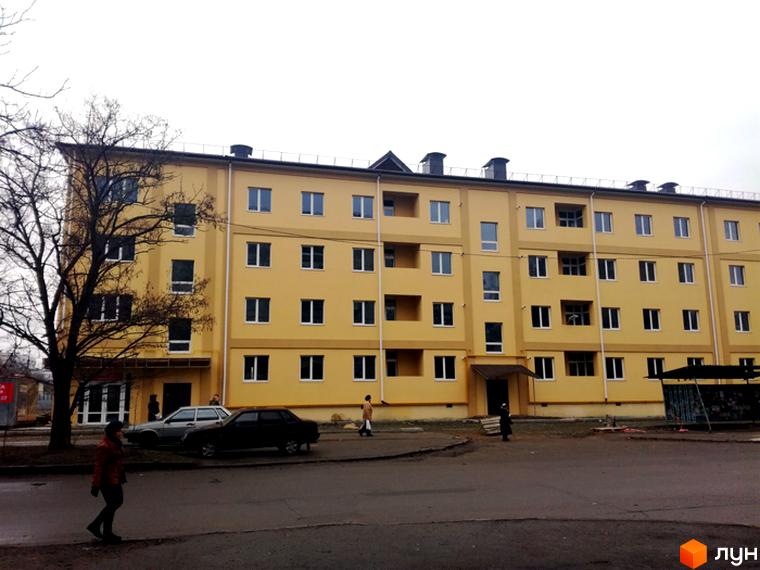 Житловий комплекс Таврійський. Багатоповерховий будинок жовтого кольору з білими вікнами. На прибудинковій території є асфальтована дорога та припарковані автомобілі.