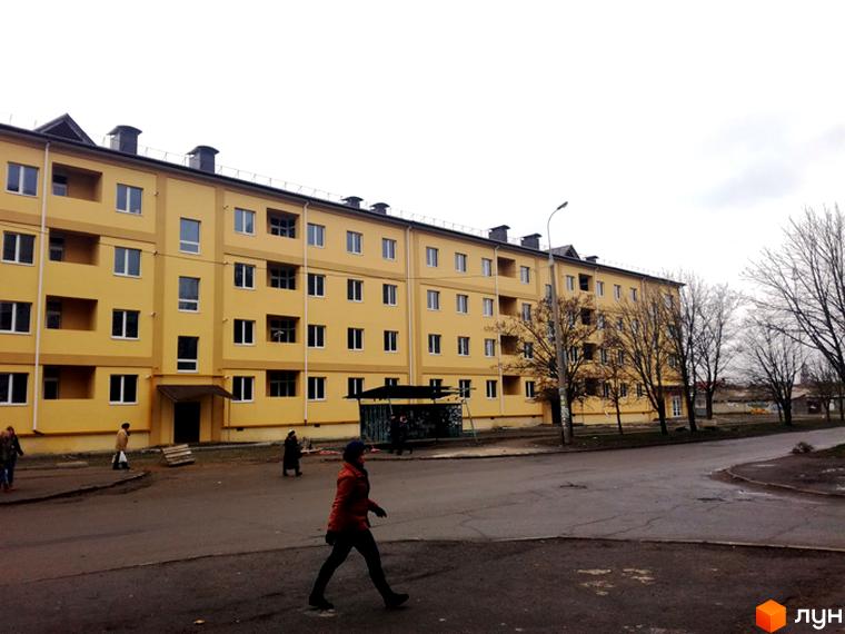 Житловий комплекс Таврійський. Багатоповерховий будинок жовтого кольору з великою кількістю вікон. На передньому плані асфальтована дорога та люди.