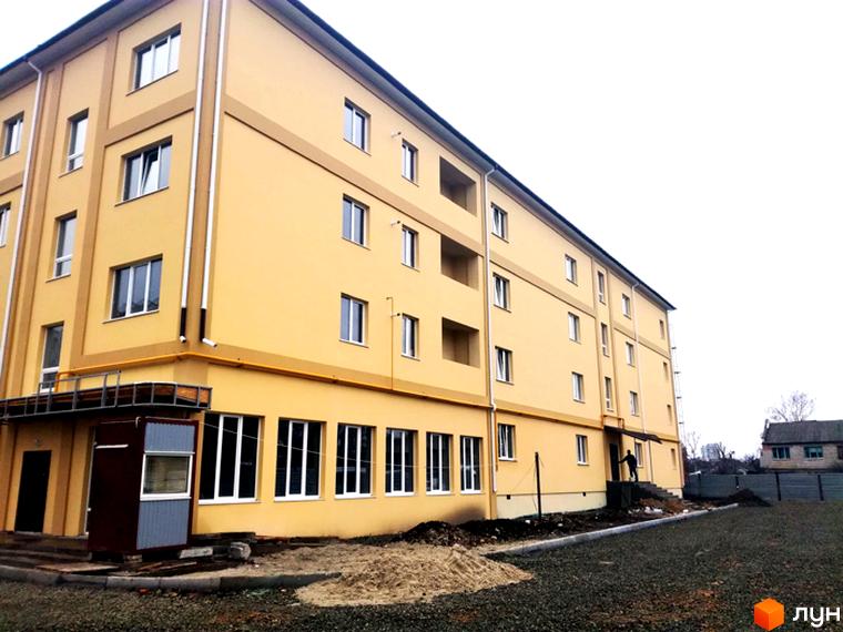 Зображення багатоповерхового будинку жовтого кольору. Поруч розташована прибудинкова територія з гравієм та огорожею.