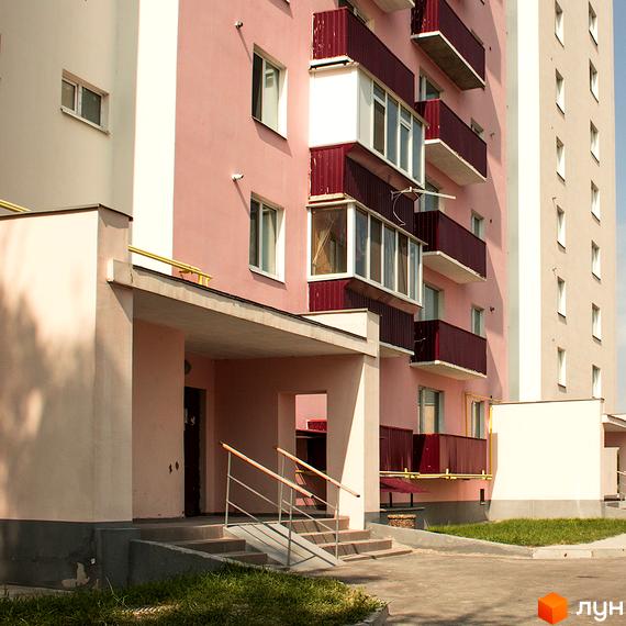 Житловий комплекс Нове Життя. Фасад будинку з рожевими та білими елементами, балконами з червоними перилами. Прибудинкова територія з газоном та доріжками.