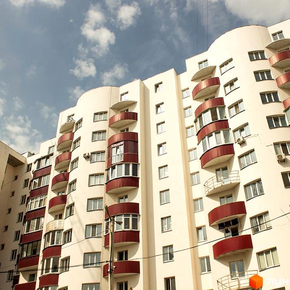 Житловий комплекс Лелека-1 з балконами та великими вікнами, прибудинкова територія з зеленими насадженнями.