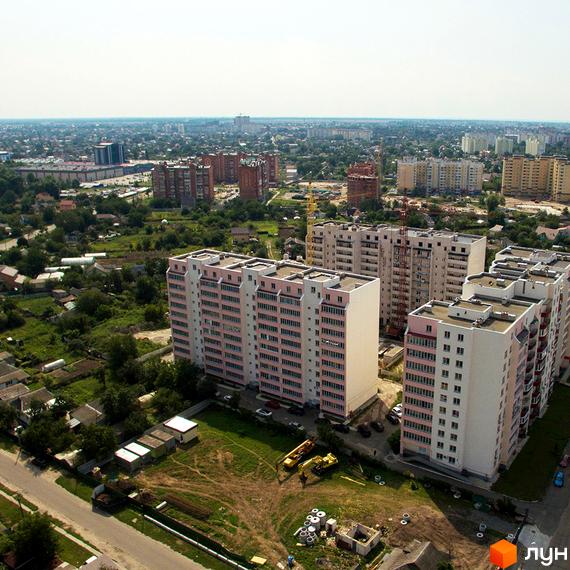 Житловий комплекс Лелека-2: багатоповерхові будинки з рожевими та білими фасадами, навколо зелена територія з дорогою та будівельною технікою.