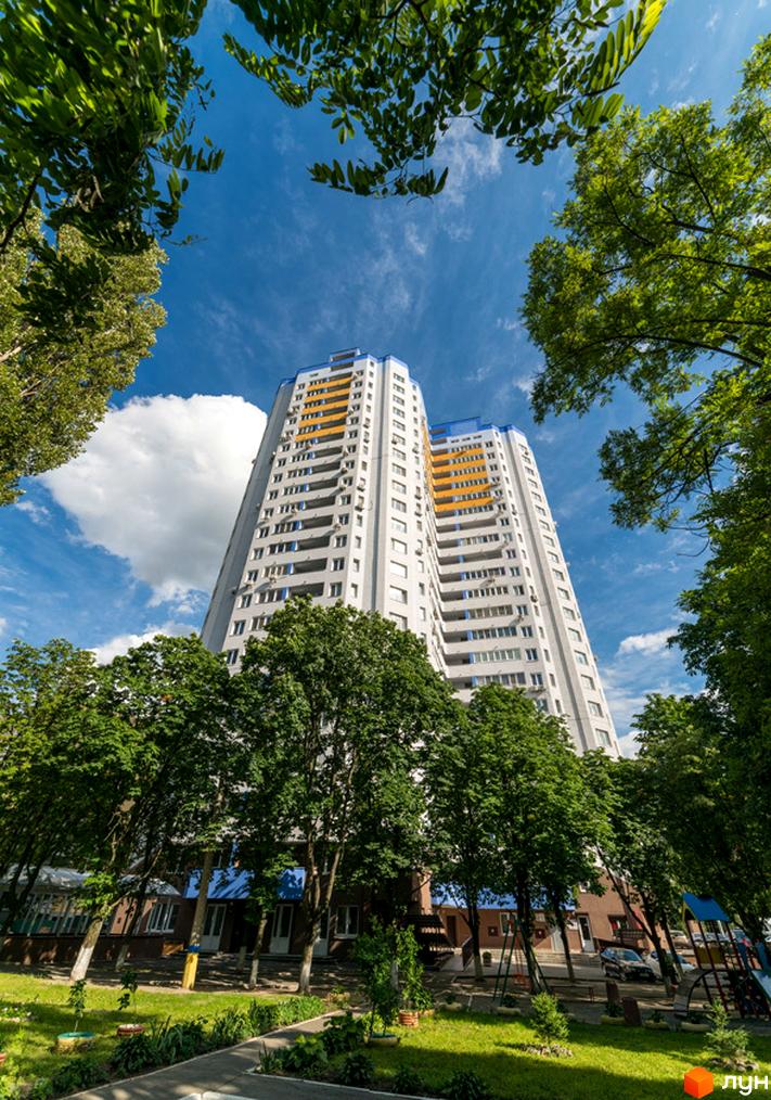 Багатоповерховий будинок ЖК Авіатор з білими фасадами, синіми та помаранчевими елементами, оточений зеленими деревами та доглянутим газоном.