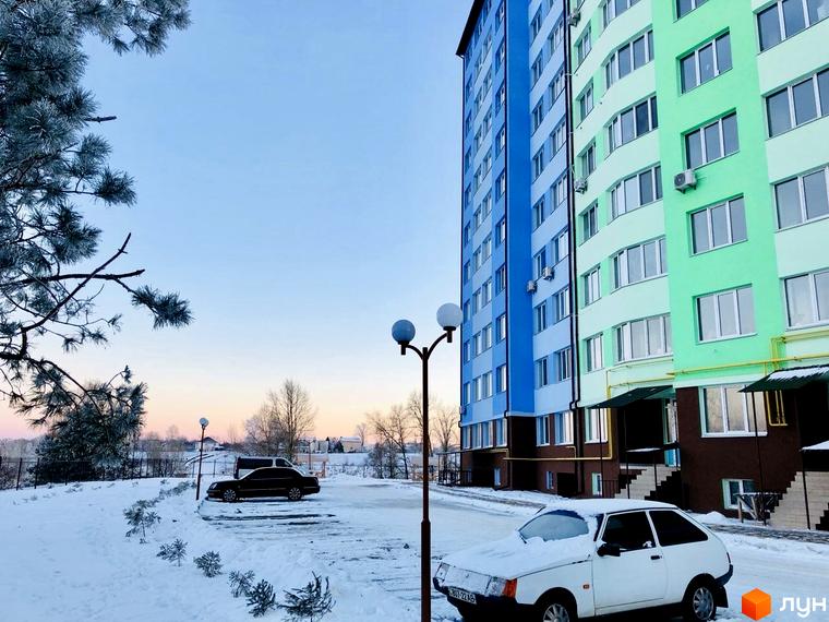 Житловий комплекс 4 Карата з яскравими фасадами синього та зеленого кольорів взимку. Навколо новобудови засніжена територія з припаркованими автомобілями та деревами.