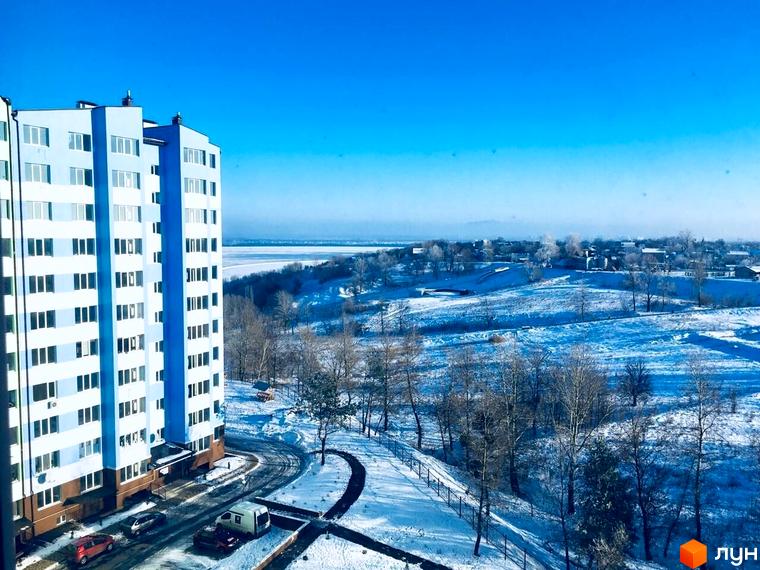 Житловий комплекс 4 Карата: світло-блакитна новобудова з білими вікнами на тлі зимового пейзажу. Навколо комплексу засніжена територія з деревами та дорогою.