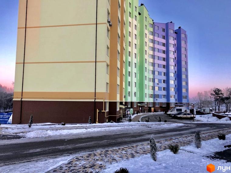 Житловий комплекс 4 Карата: яскрава багатоповерхівка з різнокольоровими фасадами взимку. Територія навколо комплексу вкрита снігом, видно дорогу та дерева.