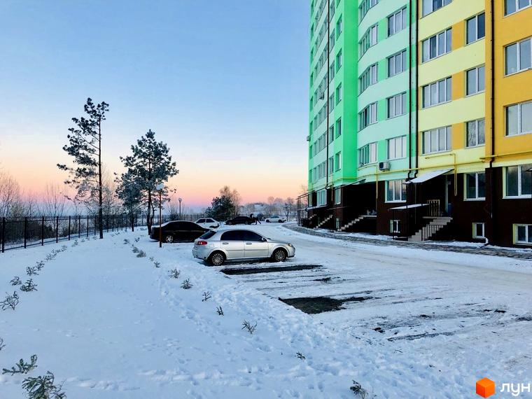 Житловий комплекс 4 Карата. Багатоповерховий будинок з яскравим фасадом у зелено-жовтих тонах, розташований на засніженій території з парковкою.