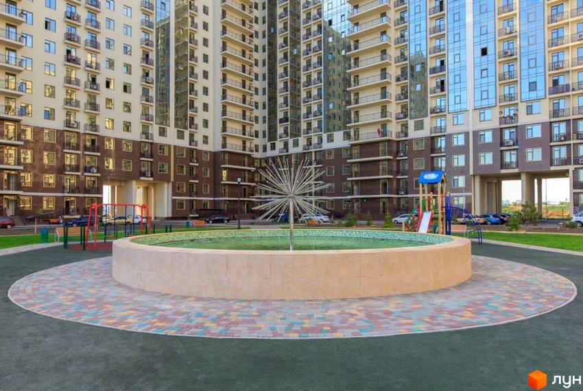Житловий комплекс Пятая Жемчужина з фасадами світлої та темно-коричневої плитки. На прибудинковій території розташовані дитячий майданчик та фонтан.