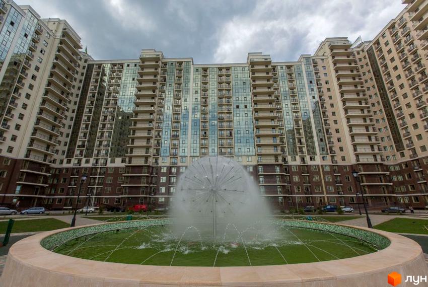 Житловий комплекс Пятая Жемчужина з фонтаном на прибудинковій території. Багатоповерхові будинки з балконами та скляними фасадами.