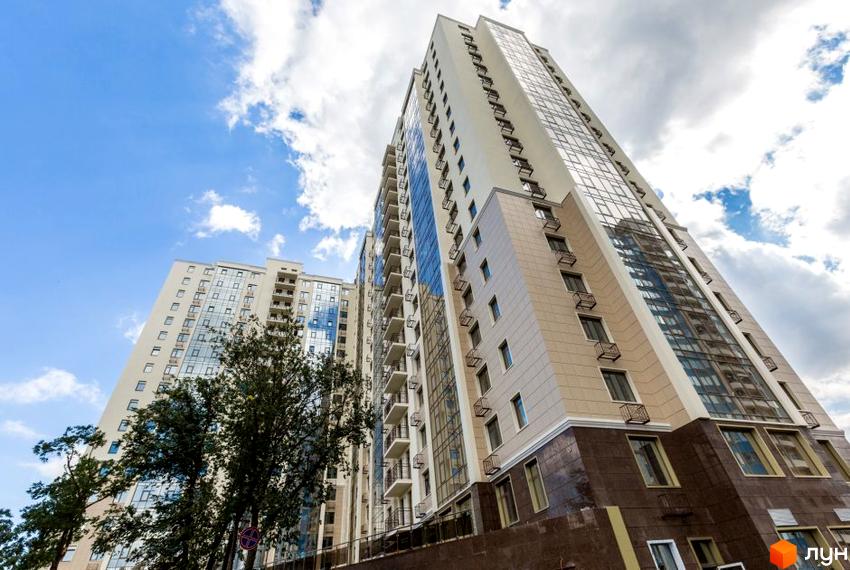 Висотна будівля Житловий комплекс Шоста Перлина на тлі блакитного неба з хмарами. Фасад будинку виконаний у світлих тонах з великими вікнами.