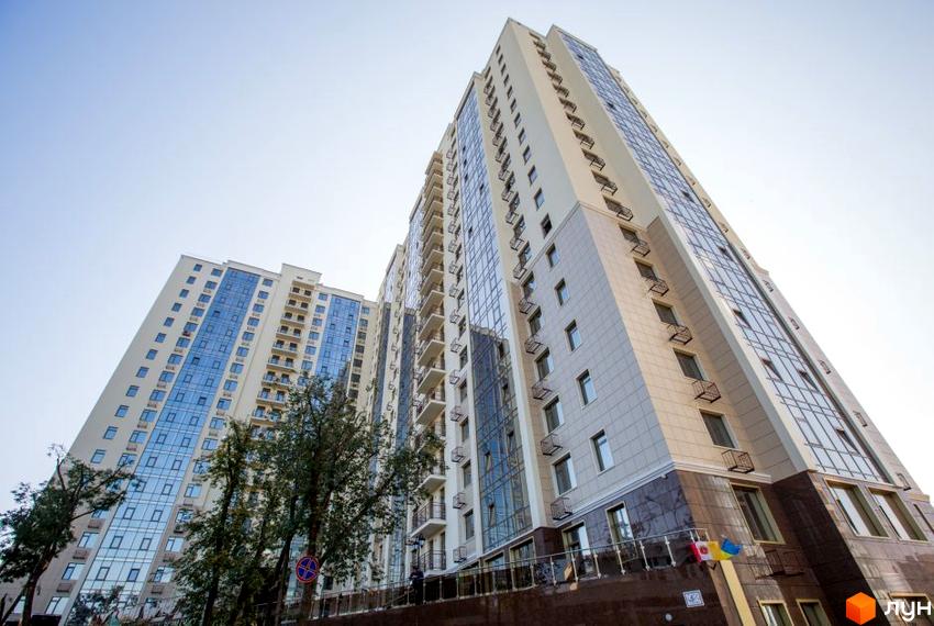 Висотна будівля ЖК Шоста Перлина з великими вікнами та балконами. На передньому плані дерева та небо.