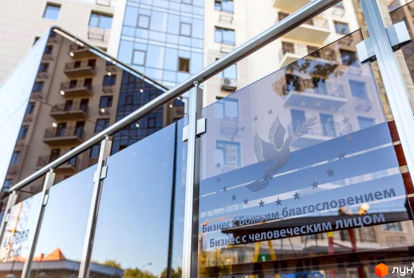 Фасад будівлі ЖК Шоста Перлина з скляними панелями. На склі зображено голуб з гілкою, що символізує мир та благословення. На передньому плані - металеві конструкції.