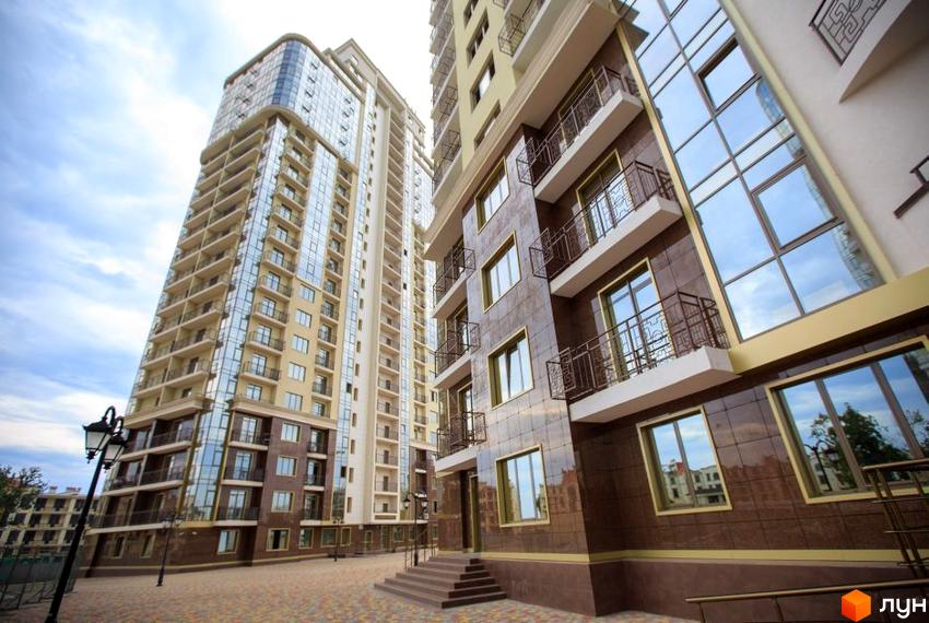 Зовнішній вигляд новобудови Восьма Перлина з фасадами з коричневої плитки та великими вікнами. Прибудинкова територія з бруківкою та ліхтарями.