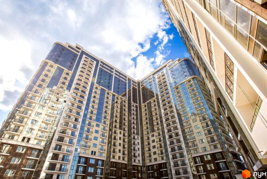 Житловий комплекс Восьма Перлина - це сучасна новобудова з панорамним склінням та балконами, що вражає своєю архітектурою. Комплекс розташований на тлі блакитного неба з хмарами.