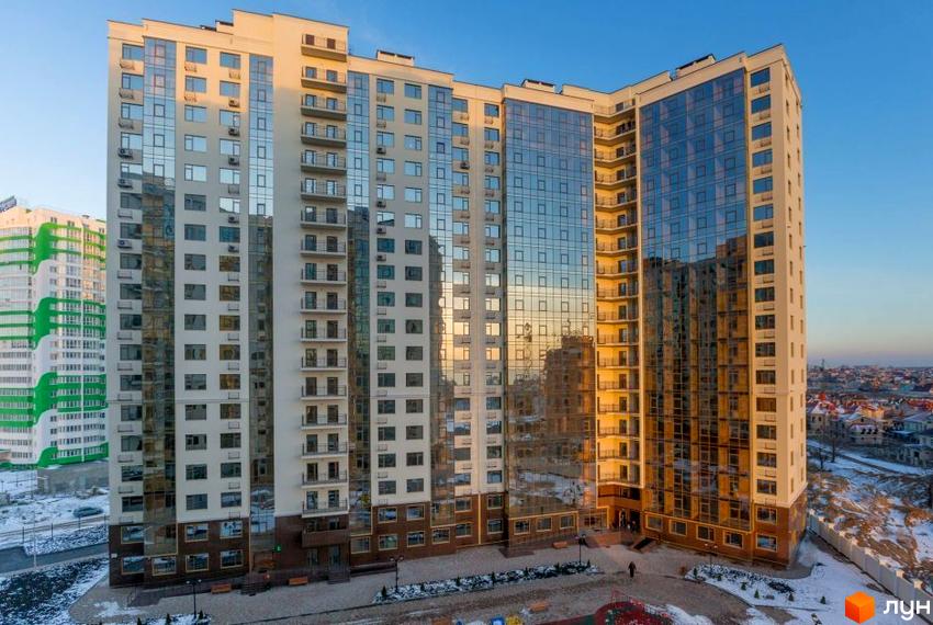 Зображення фасаду та прибудинкової території Житлового комплексу Десята Перлина. Високий багатоповерховий будинок з великою кількістю вікон.
