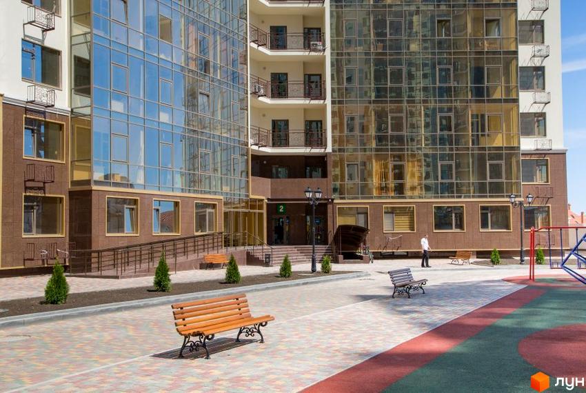 Зовнішній вигляд житлового комплексу Десята Перлина з великими вікнами та коричневим оздобленням. На передньому плані – лавки та облаштована територія.