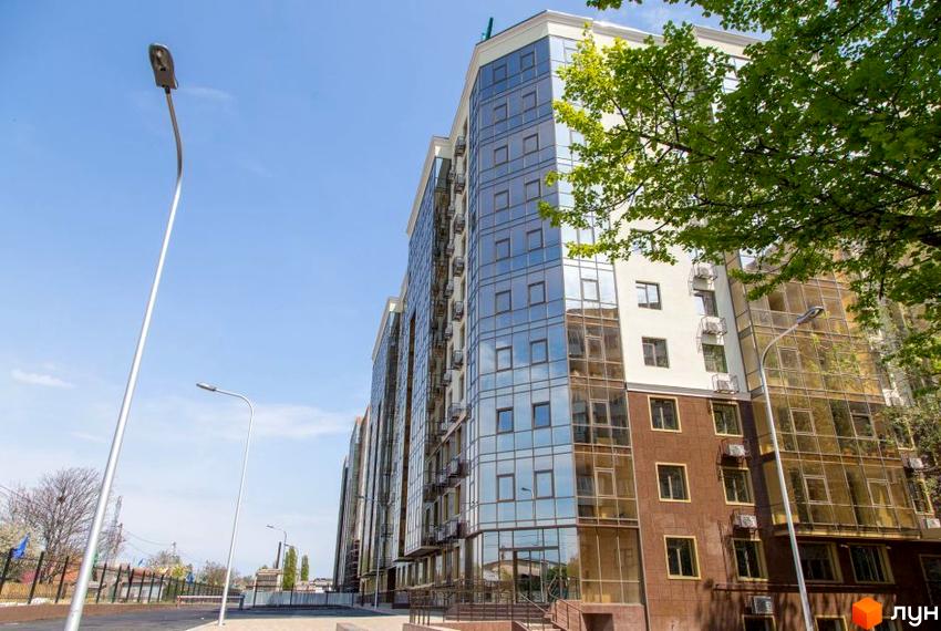 Зовнішній вигляд багатоповерхового будинку в Житловому комплексі Одинадцята Перлина. Навколо будівлі є тротуари та зелені насадження.