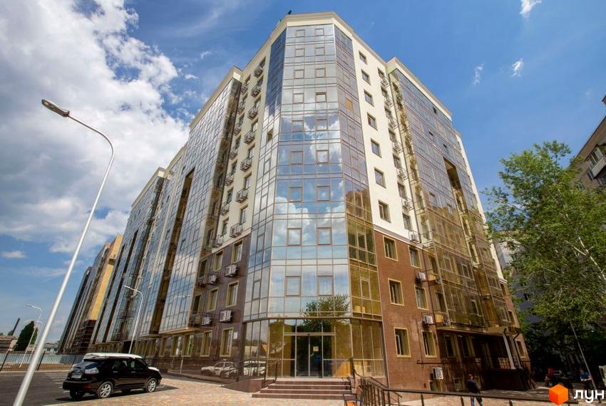 Зображення фасаду Житлового комплексу Одинадцята Перлина. Висотна будівля з панорамними вікнами та коричневим оздобленням, видно частину прибудинкової території.