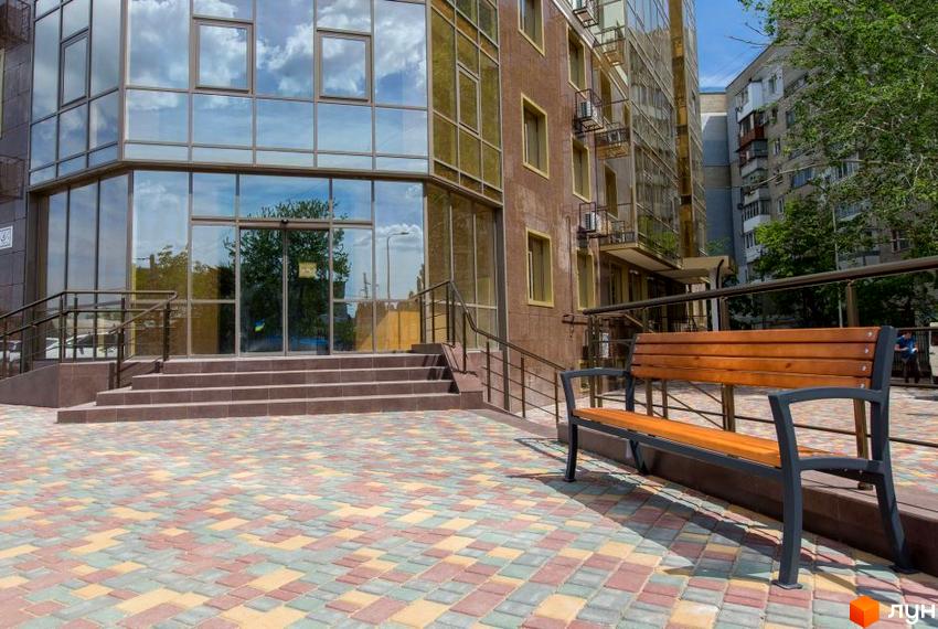 Вид на фасад та вхідну групу Житлового комплексу Одинадцята Перлина. На передньому плані лавка та кольорова тротуарна плитка.