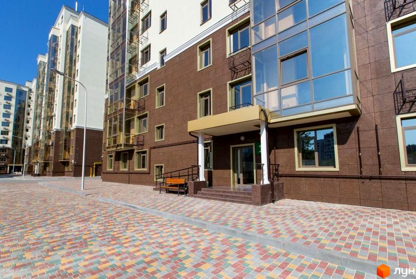 Зображення фасаду та входу у Житловий комплекс Дванадцята Перлина. На передньому плані кольорова бруківка та лавка біля входу.