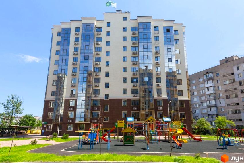 Висотна будівля Житлового комплексу Чотирнадцята Перлина з великими вікнами, що відбивають небо. Перед будинком розташований дитячий майданчик з різнокольоровими гірками та гойдалками.