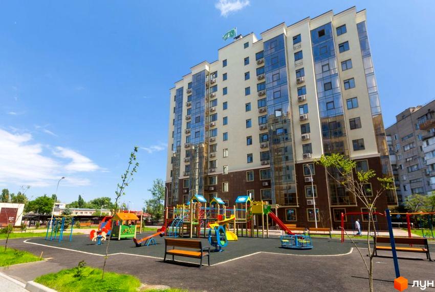 Висотна будівля ЖК Чотирнадцята Перлина з великими вікнами та балконами. На передньому плані дитячий майданчик з різнокольоровими гірками та гойдалками.