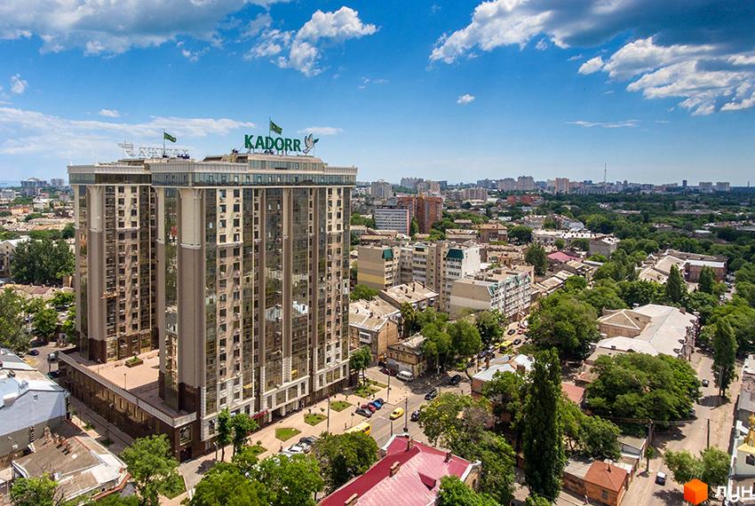 Висотна будівля ЖК KADORR з великою кількістю вікон на тлі міської забудови. На території комплексу зелені насадження та парковка для автомобілів.