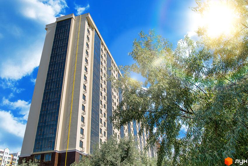 Житловий комплекс Двадцята Перлина: багатоповерховий будинок світлого кольору з темними вікнами та балконами, оточений зеленими деревами під сонячним небом.