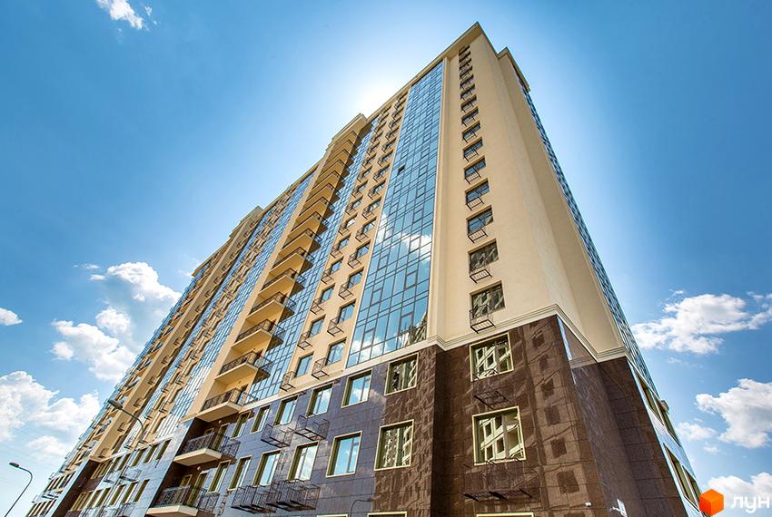 Висотна новобудова Двадцять перша Перлина з бежевим фасадом, скляними балконами та темною облицюванням нижніх поверхів.