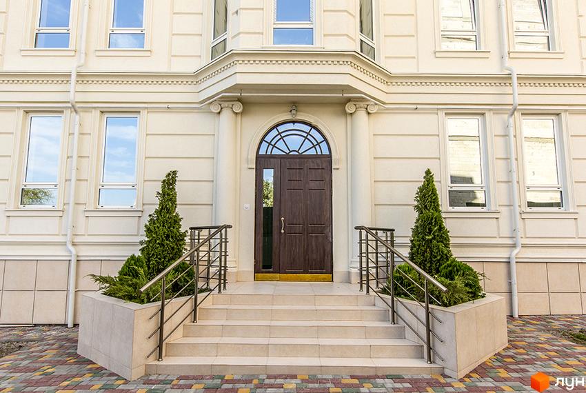 Фасад житлового комплексу Двадцять третя Перлина з парадним входом та сходами. Прибудинкова територія з зеленими насадженнями та бруківкою.