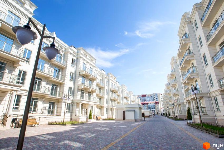 Зображення Житлового району Двадцять восьма перлина з фасадом та балконами. На передньому плані тротуарна плитка та вуличні ліхтарі.