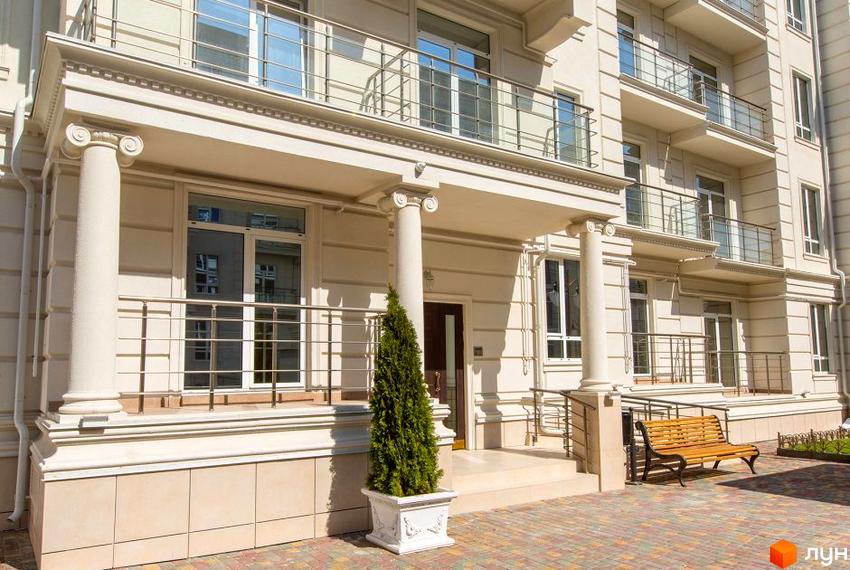 Фасад світлого будинку в Житловому комплексі Двадцять восьма перлина. На вході колони та зелена туя у вазоні, поруч лавка.