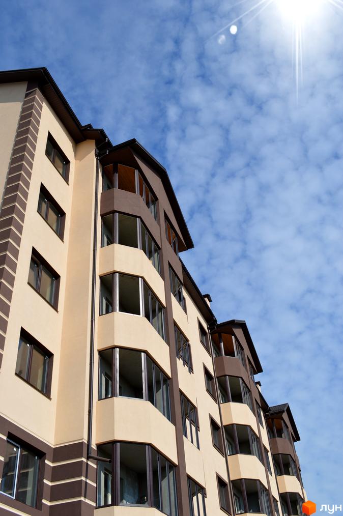 Багатоповерховий житловий будинок Житлового комплексу Сонячний з бежевим фасадом та коричневими елементами, великими вікнами та балконами на тлі блакитного неба.