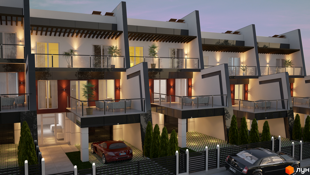 Ряд багатоповерхових таунхаусів „Капітель“ з балконами та скляними огорожами. Перед будинками є доріжки, зелені насадження та паркувальні місця.