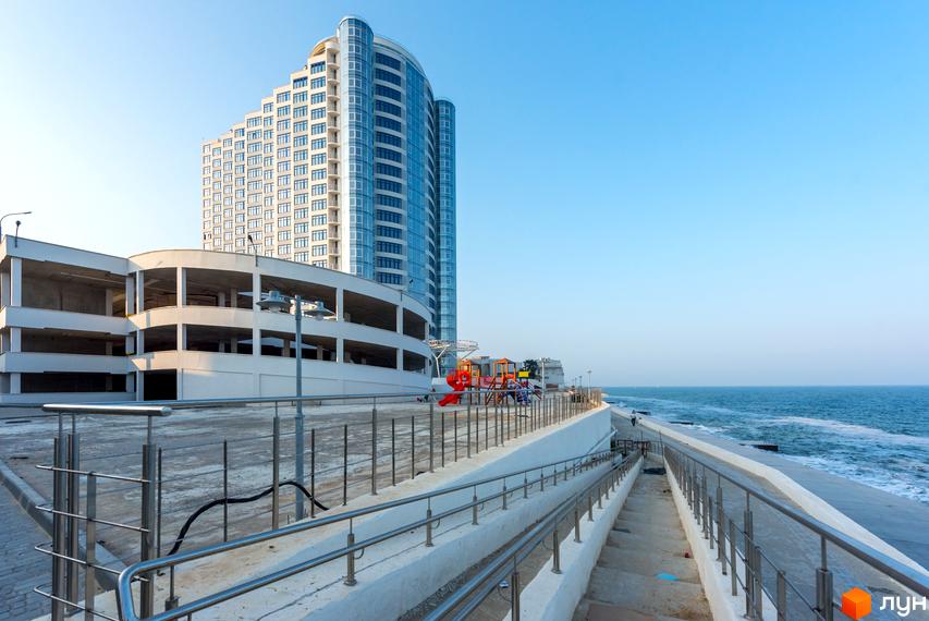 Житловий комплекс Морська симфонія з висотним будинком та прибудинковою територією біля моря. Вид на парковку та дитячий майданчик.