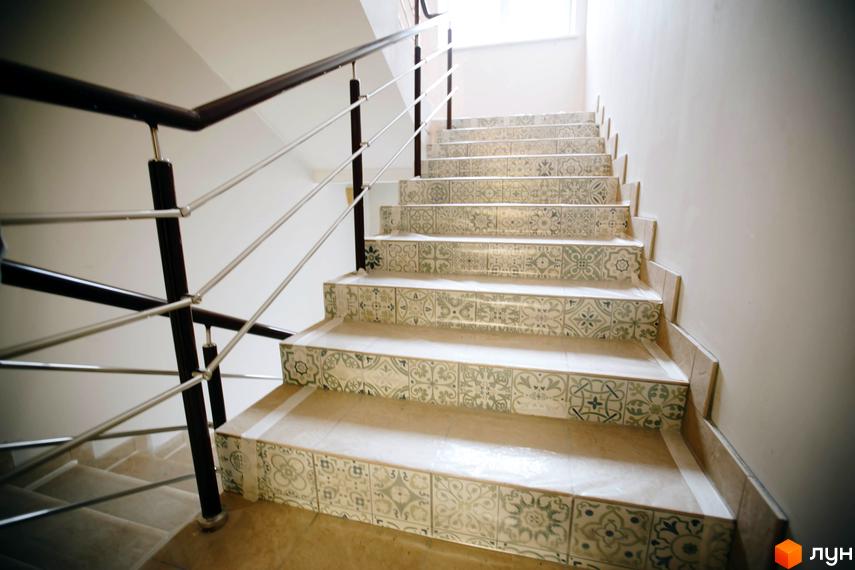 Сходи в ЖК Comfort Club з візерунчастою плиткою на підсходинках. Поручні з дерева та металу, чистий простір.