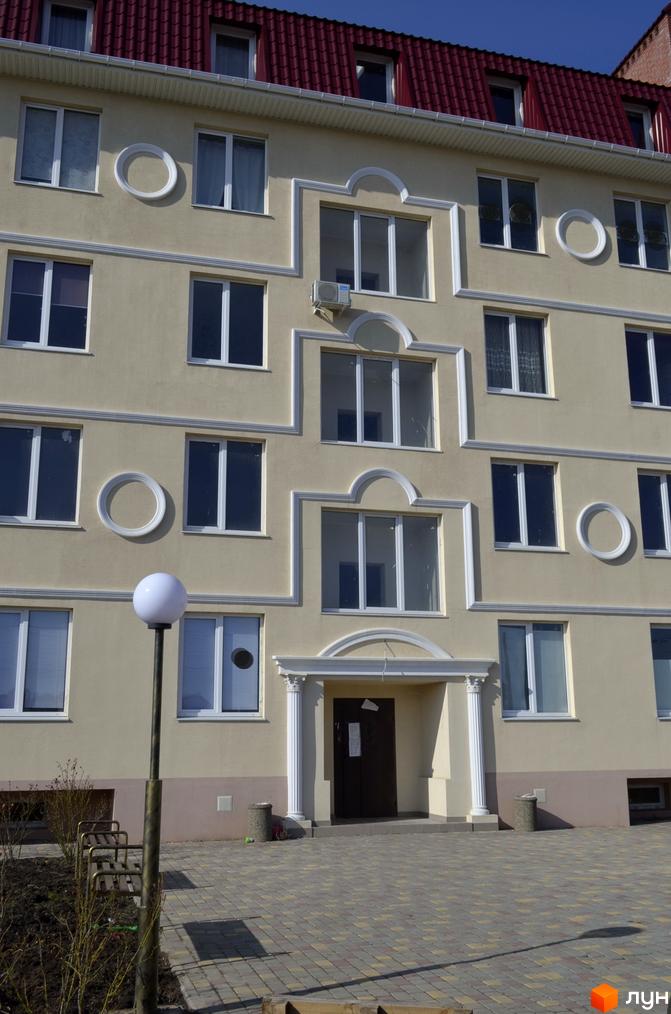 Фасад житлового комплексу Зелений гай з вікнами та декоративними елементами. Перед будинком розташована прибудинкова територія з лавками та ліхтарем.