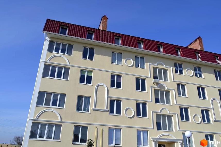 Фасад житлового комплексу Зелений гай з червоним дахом та численними вікнами. Будинок має світло-жовтий колір та білі декоративні елементи.